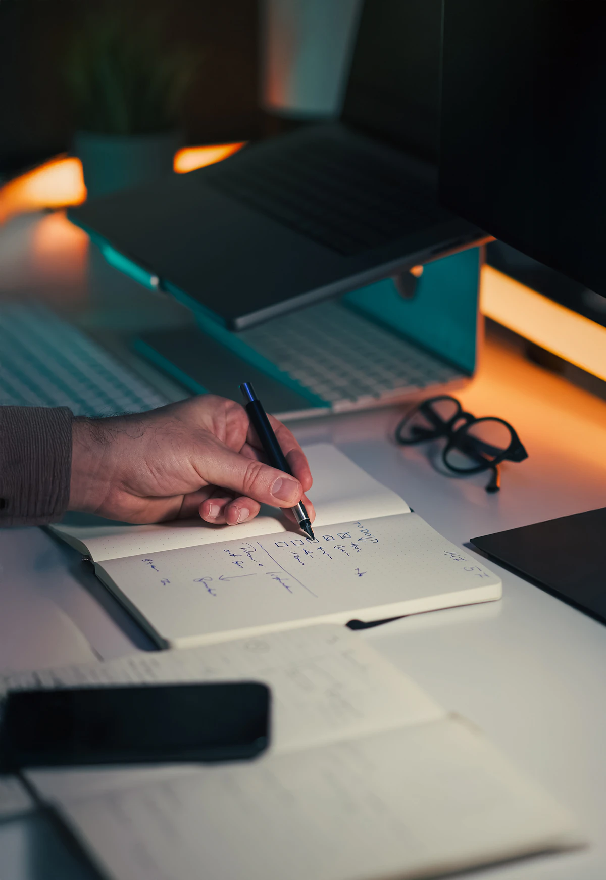A hand recording notes beside a laptop